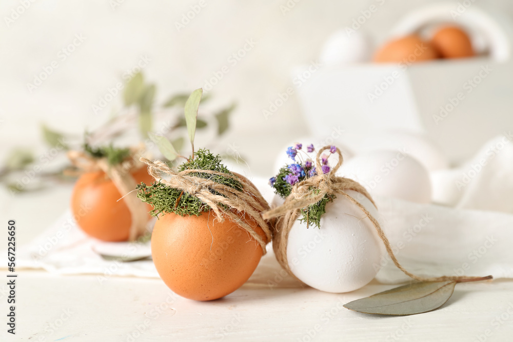 Easter eggs with tied moss and flowers on white table
