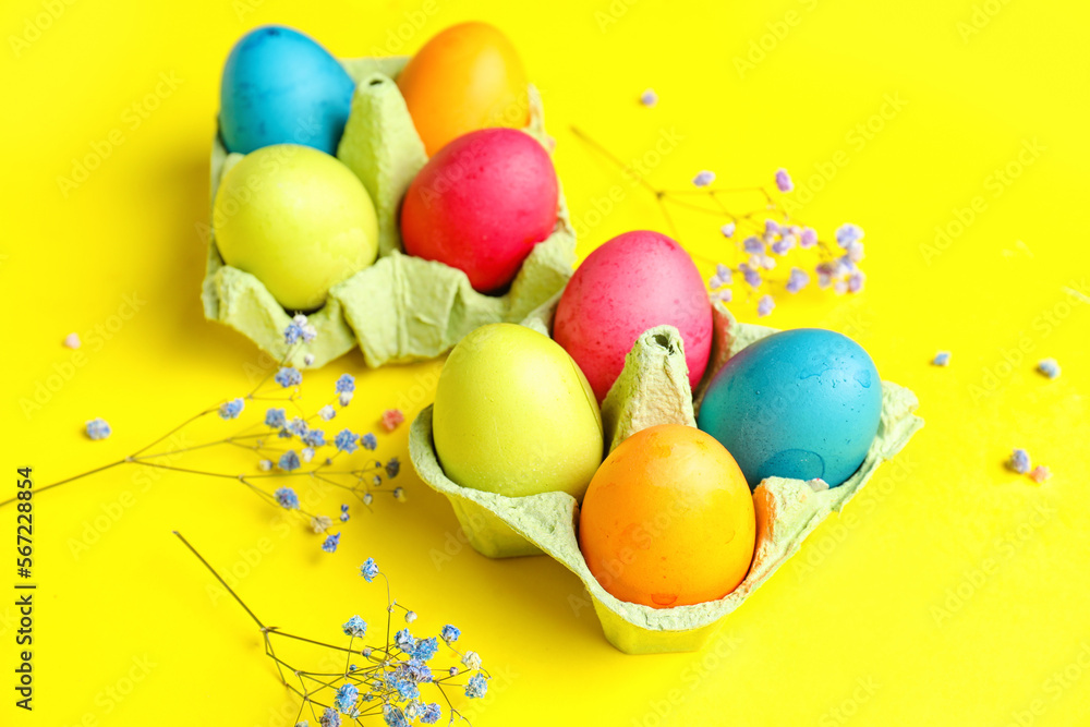 Cardboard holders with painted Easter eggs and gypsophila flowers on yellow background
