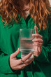 Unrecognizable woman in a green shirt holding a ribbed glass of water