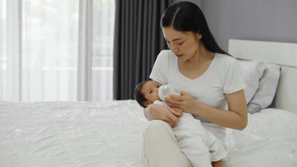 Wall Mural - mother feeding milk bottle to her newborn baby on a bed