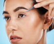 © Wesley JvR/peopleimages.com - Hair removal, tweezer and woman doing her eyebrows in studio for beauty, facial and grooming routine. Cosmetics, depilation and female model plucking face hair with cosmetic tool by blue background.