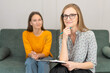 © Volha - Smiling female psychologist with glasses looks into the camera, consulting a smiling young woman in the office interior. Therapy, mental problems, psychological support and professional help
