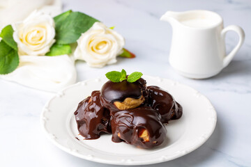 Wall Mural - Delicious profiteroles with chocolate and white plate. Selective focus image on light background.