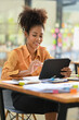 © Prathankarnpap - Smiling African American female employee searching online information on digital tablet, sitting at her workplace
