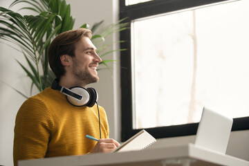 Canvas Print - Portrait of a happy man taking notes while using laptop in office.