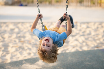 Wall Mural - Swinging on playground. Happy child enjoy swinging. Kid swinging. Happy little child having fun on swing in playground. Cute child swinging on sunny spring day.