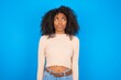 © Jihan - Displeased Young woman with afro hair style wearing crop top over blue background frowns face feels unhappy has some problems. Negative emotions and feelings concept