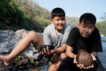 Asian boys are spending their freetimes by sitting on stones, diving, swimming, throwing rocks and catching fish in the river together happily. Hobby and happiness of children concept.