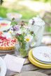 Tisch im Grünen gedeckt mit Erdbeerkuchen und Tellern, einer alten Kaffeekanne und einem Strauß Wiesenblumen