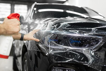 Worker Applies A Protective Film Or Anti-gravity Protective Coating To The Car Headlight. Details Of The Car.