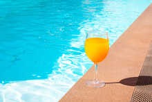 The Orange Juice In The Wine Glass Is Beside The Swimming Pool.