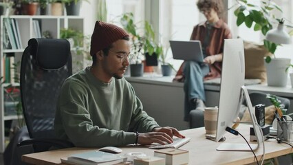 Young developer sitting at his workplace in front of computer monitor and working with computer program