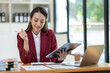 © crizzystudio - Beautiful attractive Asian businesswoman holding a clipboard of documents sitting analytically analyzing various marketing management information the finances were at her desk in the office at ease.