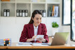 © crizzystudio - Asian businesswoman working at office pressing calculator to calculate and writing company account on graph paper. Review various information and management concepts.