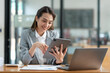 © crizzystudio - Asian businesswoman in a suit sitting holding iPad or tablet in contact See details and discuss business information happily in the office.
