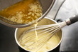 Cooking process of hollandaise sauce, pouring melted butter into the pot with egg mixture, whisking all the time at low temperature to get a creamy texture, selected focus