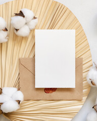 Wall Mural - Blank card and envelope on dried palm leaf with cotton flowers top view, wedding mockup