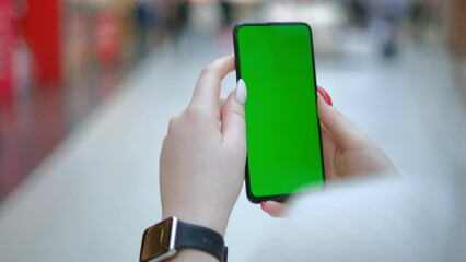 Mall. Beautiful Female using Mobile Phone. Back view of brunette holding chroma key green screen smartphone watching content. Shopping online. Gadgets and contemporary people concept.4K
