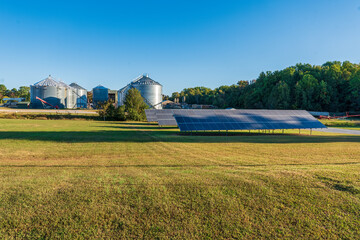 Solar panels on a grain farm with grain bins and a saw mill in the background on a sunny day in Vantown, Tennessee.