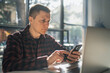 © DedMityay - Man using modern smartphone and looks at screen sitting in cafe.