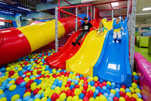 Happy Kids Playing At Indoor Play Center Playground. Children Slides In Colored Slide Into Balls In Ball Pool.