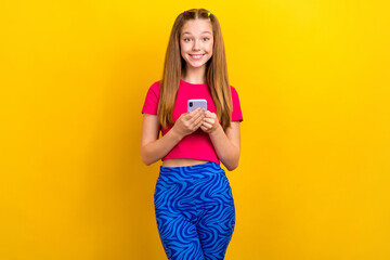 Poster - Photo of satisfied schoolgirl blond hair pink t-shirt hold phone facebook instagram twitter whatsapp isolated on yellow color background