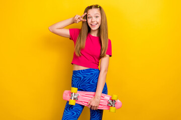 Sticker - Photo of optimistic cheerful schoolgirl straight hairdo pink t-shirt showing v-sign hold skateboard isolated on yellow color background