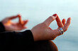 © robertharding - Woman practising yoga meditation by the sea at sunset as concept for silence and relaxation, close-up on hand, gyan mudra, Spain, Europe