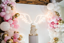 Celebration Baptism Concept. Arch Decorated With Pink, White, Golden Balloons, Angel Wings. Trendy Cake With Decor. Reception At Birthday Baby Party On Wall. Delicious Reception On Photo Zone, Area.