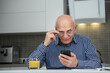 © Bonsales - Elderly male person using smart phone sitting at kitchen table