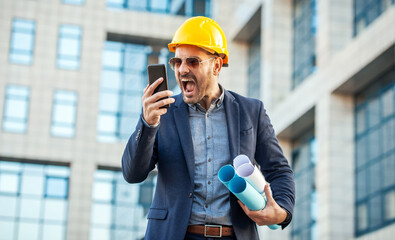 Something is wrong on building site. Angry architect yelling on head of the construction site while talking with him via mobile phone. Construction concept