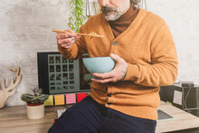 Close-up Of Freelancer Eating Oriental Food, Holding Rice With Chopsticks, Resting At Office Desk, Worker Enjoying Asian Food At Workplace During Lunch.