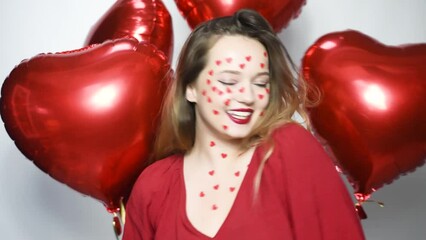 Wall Mural - A woman with heart stickers on her face. The girl on the background of red balloons in the shape of a heart. Love, feelings. The girl dances, laughs, air kisses.