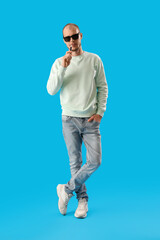 Wall Mural - Young man in sunglasses with disposable electronic cigarette on blue background