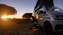 Man Sitting With Digital Device At His Transporter Camping Van Bus At The California Ocean In The Coastal Nature - Digital Nomades Concept