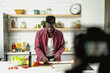 © JustLife - African man filming cooking vlog. Happy man filming his blog about healthy food at home.