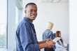 © baranq - Portrait of young African American man standing with digital tablet in coworking office smiling at camera