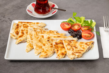 Traditional Turkish flatbread or Gozleme with tomatoes, olives and tea on dark stone table