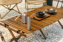 Stainless Steel Kettle, Chair,portable Gas Stove, Bowl And Vintage Lanterns On Outdoor Wooden Table In Camping Area