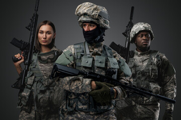 Shot of brave military people dressed in uniform holding rifles against gray background.