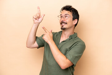 Young caucasian man isolated on beige background pointing with the index finger a great idea