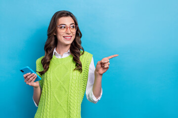 Wall Mural - Photo of charming cheerful girl hold telephone look direct finger empty space isolated on blue color background