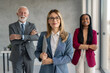 © Dorde - Satisfied and proud businesswoman team leader holding laptop standing with her colleagues looking at camera. Diverse business corporate team posing together in modern office for group business photo.
