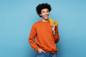 Wall Mural - Portrait of smiling African American man wearing stylish clothes isolated on blue background, copy space. Happy attractive fashion model with curly afro hair posing for photo, studio shot 
