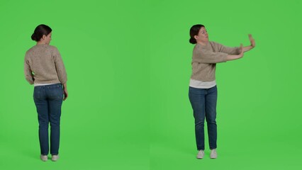 Wall Mural - Displeased woman doing pushing action on camera, trying to push something outside standing over full body greenscreen backdrop. Discontent girl moving thing in studio, expressing rejection.