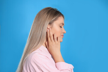 Wall Mural - Young woman suffering from ear pain on light blue background. Space for text