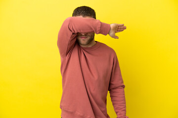 Wall Mural - Handsome blonde man over isolated yellow background covering eyes by hands