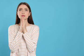 Wall Mural - Woman with clasped hands praying on turquoise background, space for text