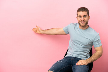 Poster - Young man sitting on a chair over isolated pink background extending hands to the side for inviting to come