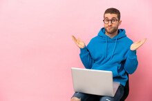 Young Man Sitting On A Chair With Laptop Having Doubts While Raising Hands